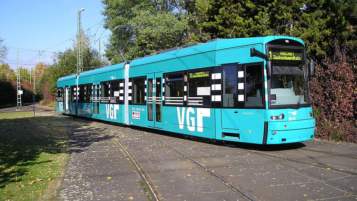 VGF-Bahn beim schönen Wetter mit Bäumen und Wiese rechts und links der Schienen
