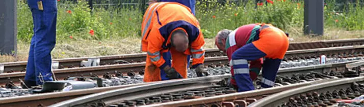 Bauarbeiter in orangener Arbeitskleidung beim Arbeiten an den Schienen