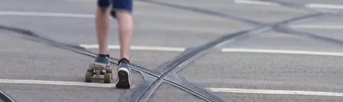 Junge mit Skateboard, der inmitten von Straßenbahnschienen fährt