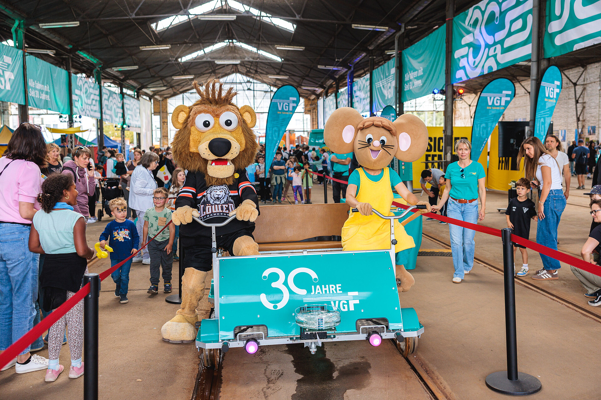 Die Maskottchen der VGF, die Maus Lisa, und der Frankfurt Lions, ein Löwe, fahren gemeinsam Draisine auf der 30 Jahre VGF-Feier