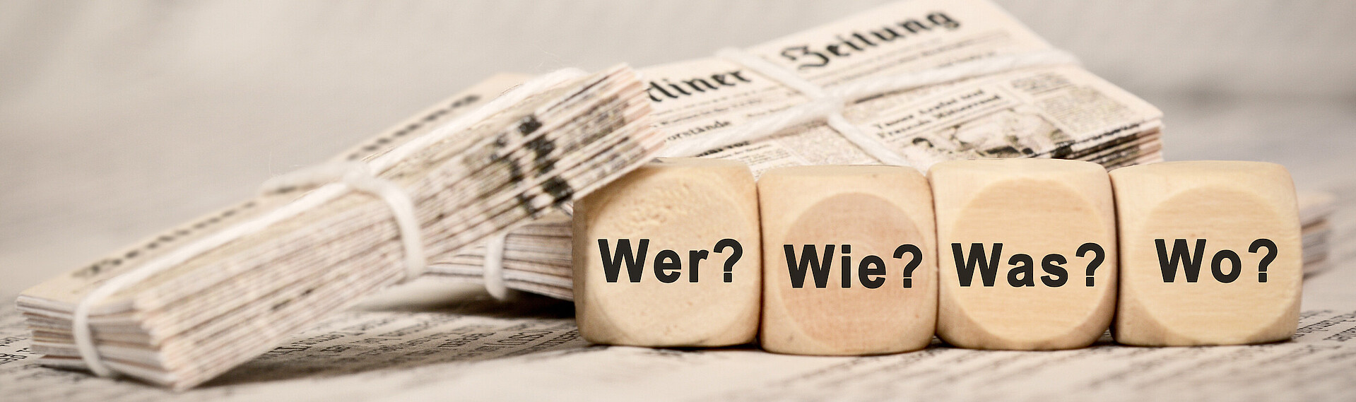 Zeitungen im Bild und Holzwürfel mit den Fragen Wer, Wie, Was, Wo