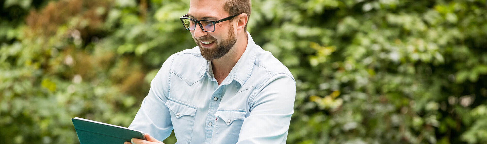 Semesterticket Header Das Bild zeigt einen jungen Mann, der in einem Park auf einer Decke sitzt und auf sein Tablet schaut.