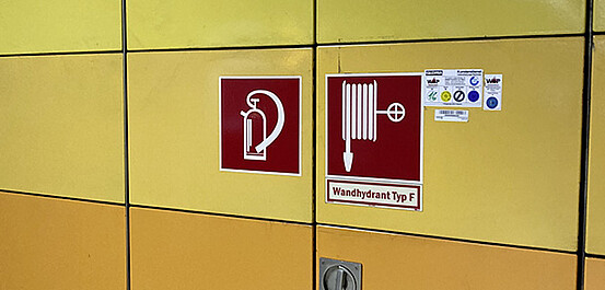 Das Bild zeigt ein Piktogramm für Feuerlöscher und Hydrant an der Wand in einer U-Bahnstation.